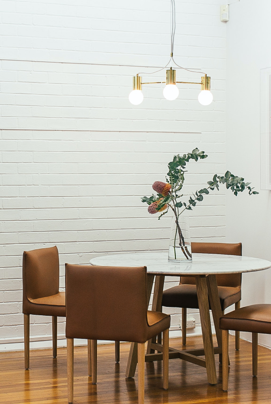 a dining table with 4 chairs. a hanging lamp. there is a flower pot in the centre of the table.